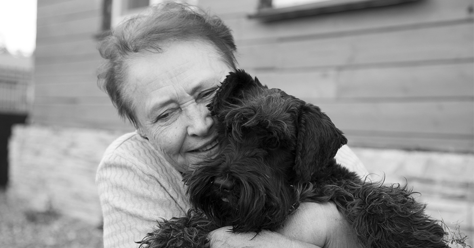 Pet Ownership and Effect on Mental Health in Seniors. Black and White picture of an elderly caucasian female hugging a small black dog.