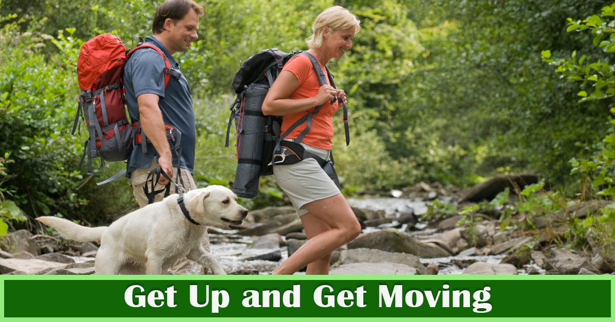Get Up and Get Moving – for Health’s Sake! Picture of a young caucasian male and female hiking outside with a blonde labrador retriever.