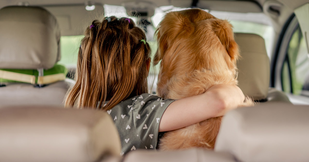 Image of little girl with arm around dog in back seat of car